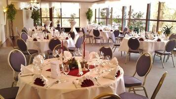 A banquet hall with round tables set for dining, featuring white tablecloths, red napkins, and gold-rimmed chairs.