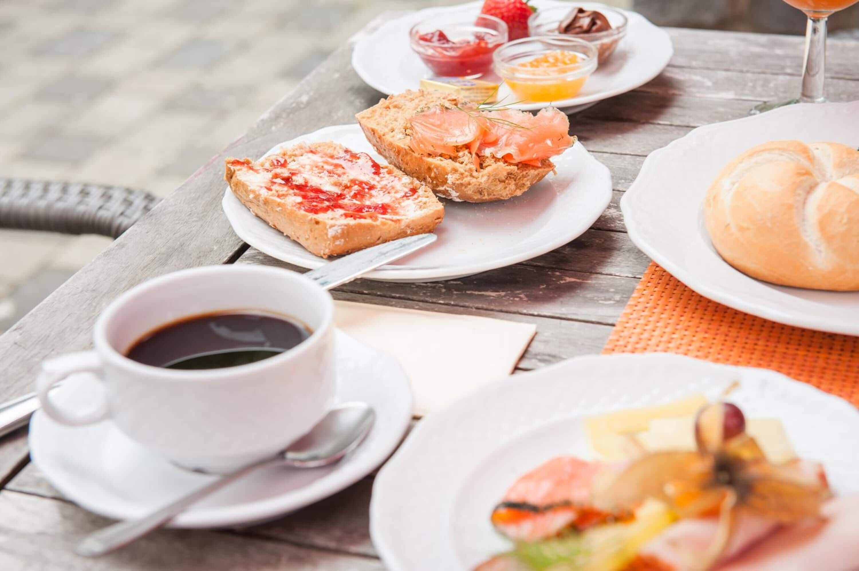 A wooden table with breakfast items including toast, salmon, jam, and a croissant.