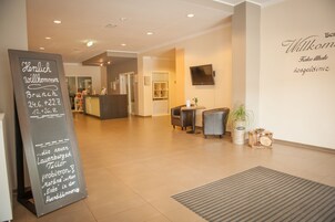 A hotel reception area with a chalkboard sign, a reception desk, seating area, and a wall-mounted TV.