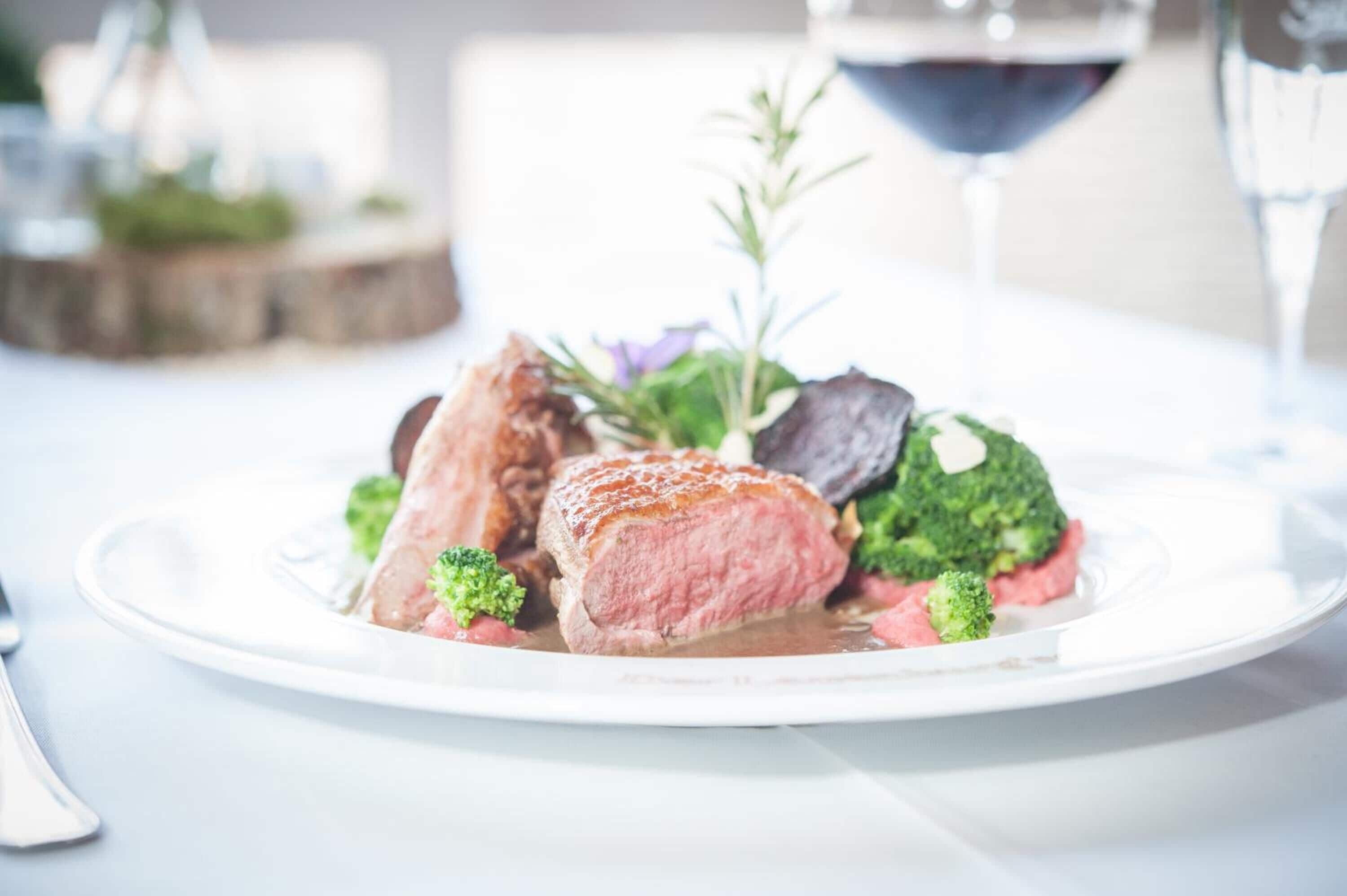 A plate of food with meat and vegetables, a glass of red wine, and a fork on a table.