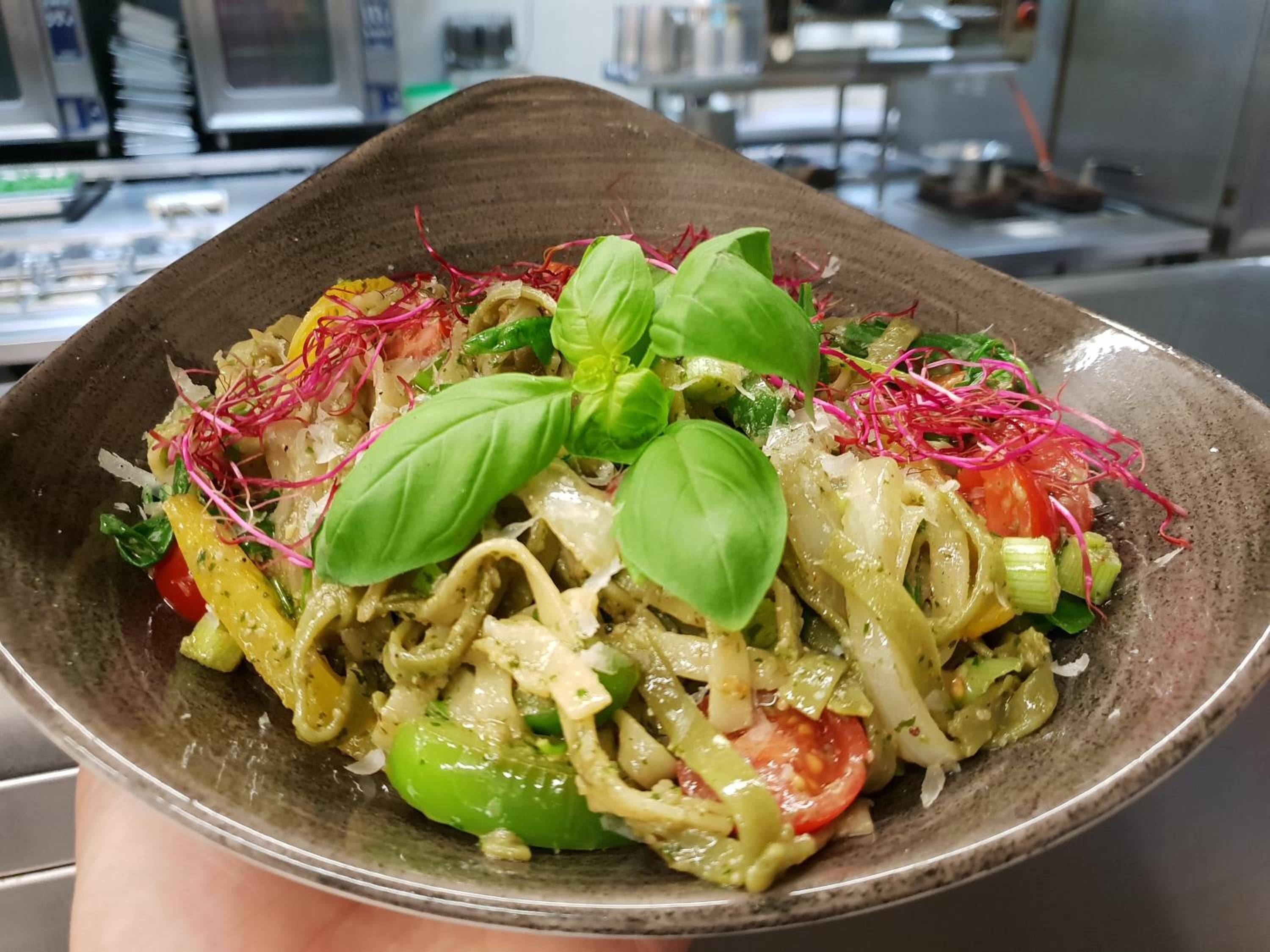 A bowl of pasta with vegetables and basil leaves.