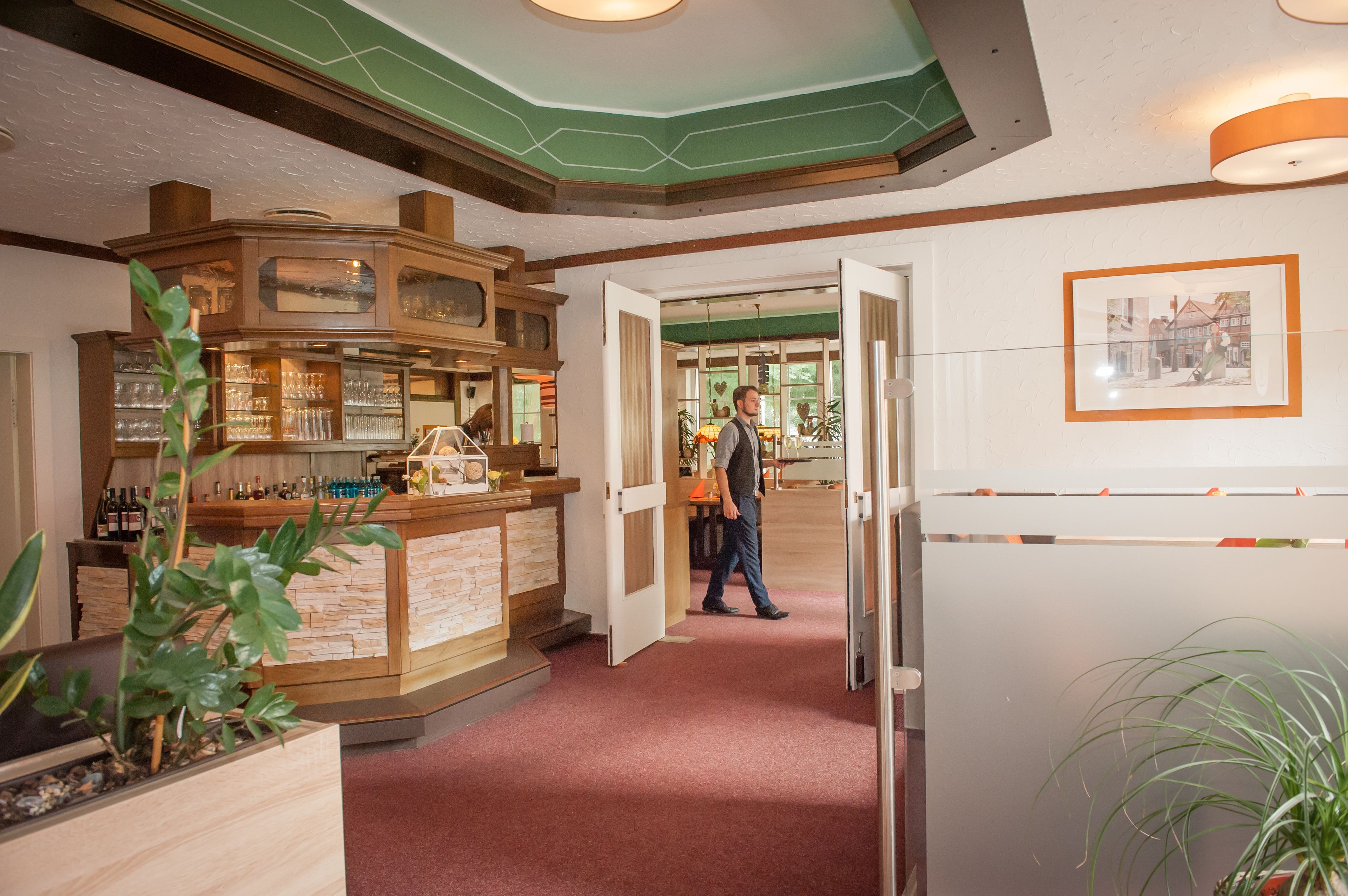 Un hall d’hôtel avec un comptoir d’accueil en bois, une moquette rouge et un tableau encadré au mur.
