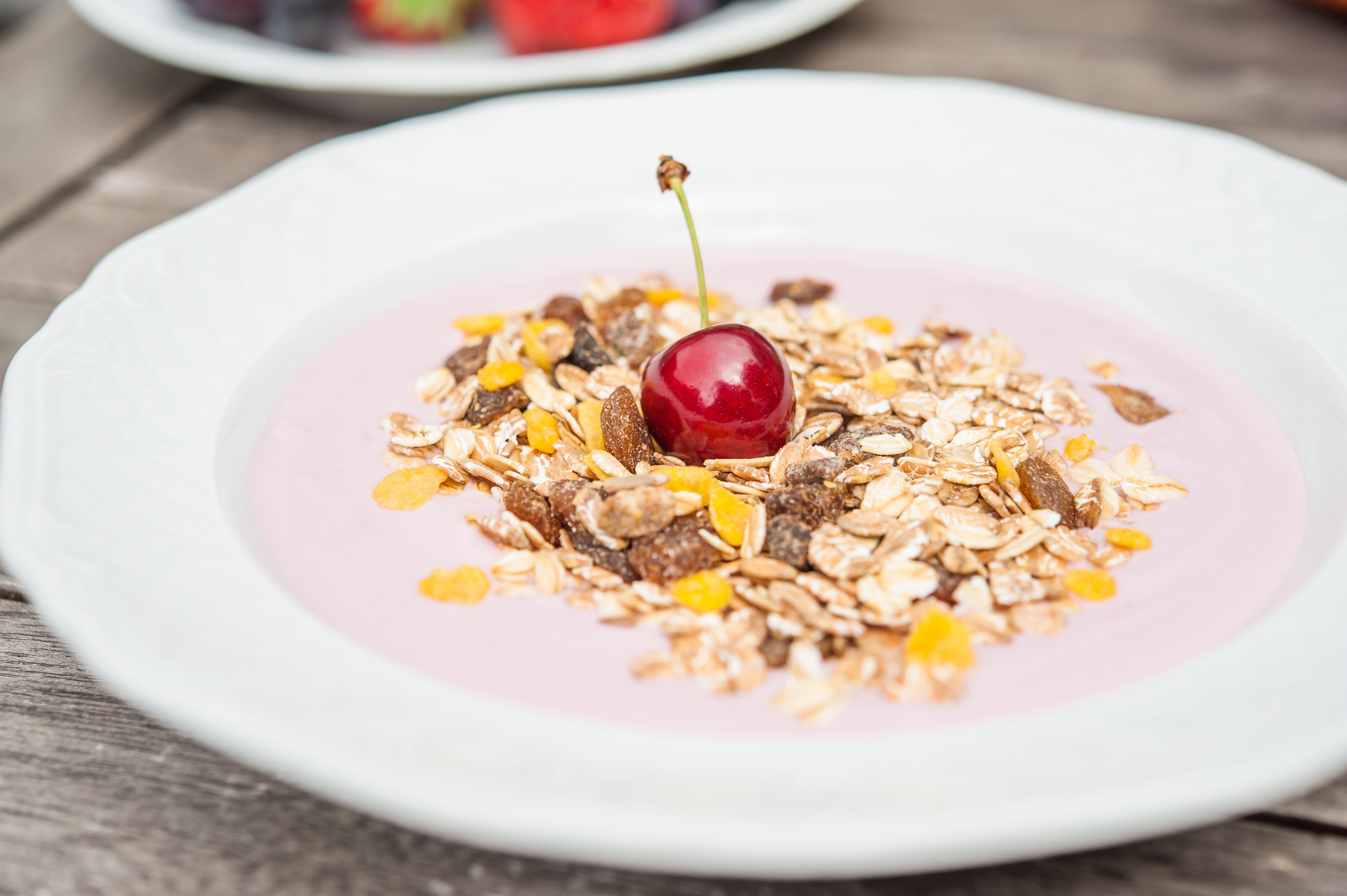 A white plate with a pinkish dessert topped with granola and a cherry.