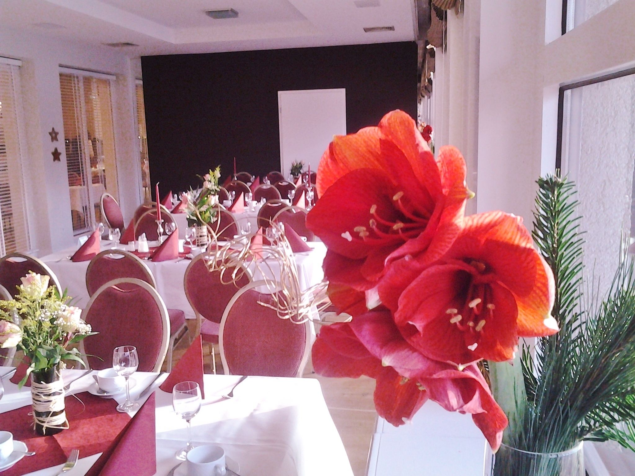 A banquet hall with round tables set for a formal event, featuring white tablecloths, red chairs, and floral centerpieces.