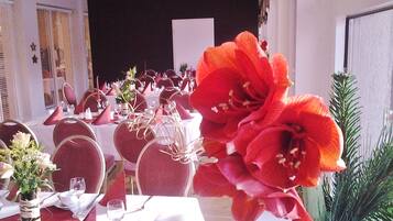 Un salón de banquetes con mesas redondas dispuestas para un evento formal, con manteles blancos, sillas rojas y centros de mesa florales.