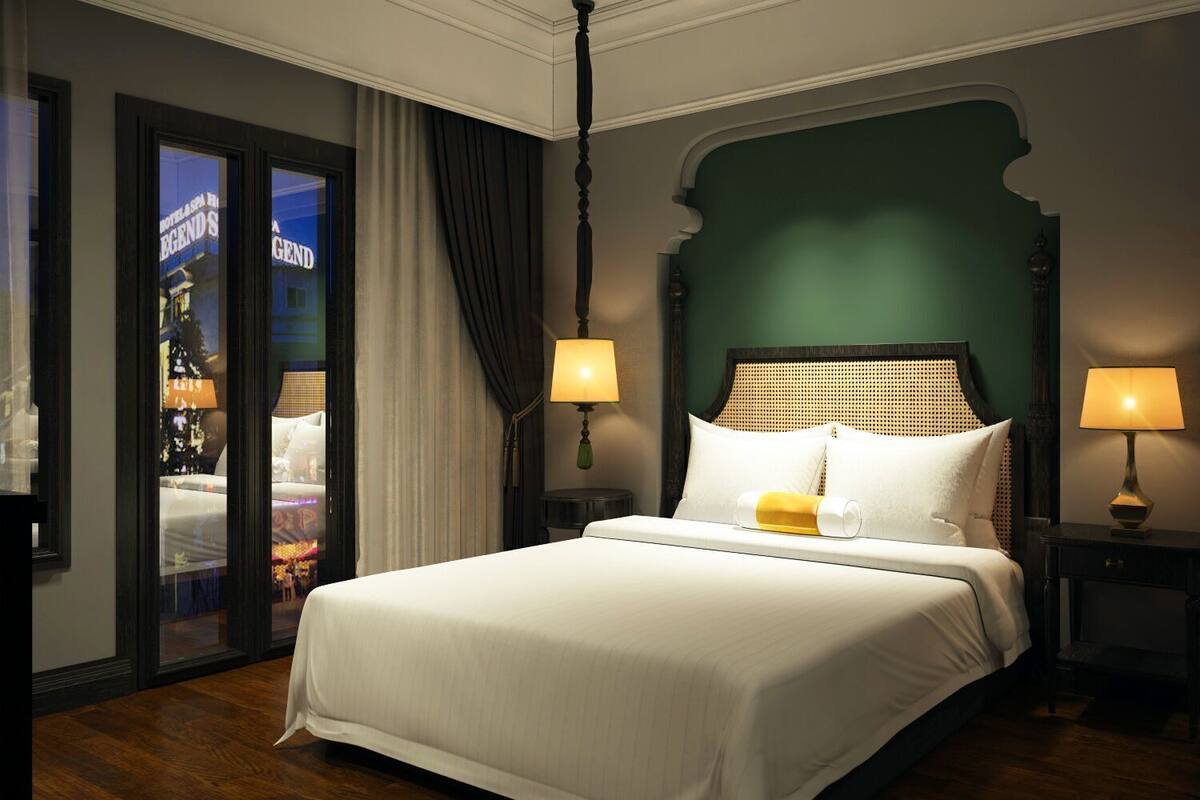 Habitación de hotel con una cama grande, dos lámparas de noche, una pared de acento verde y vistas a través de una puerta de cristal.