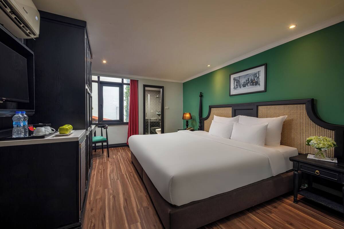 Una habitación de hotel con una cama grande, un escritorio con una silla, una ventana con cortina roja y una pared verde.