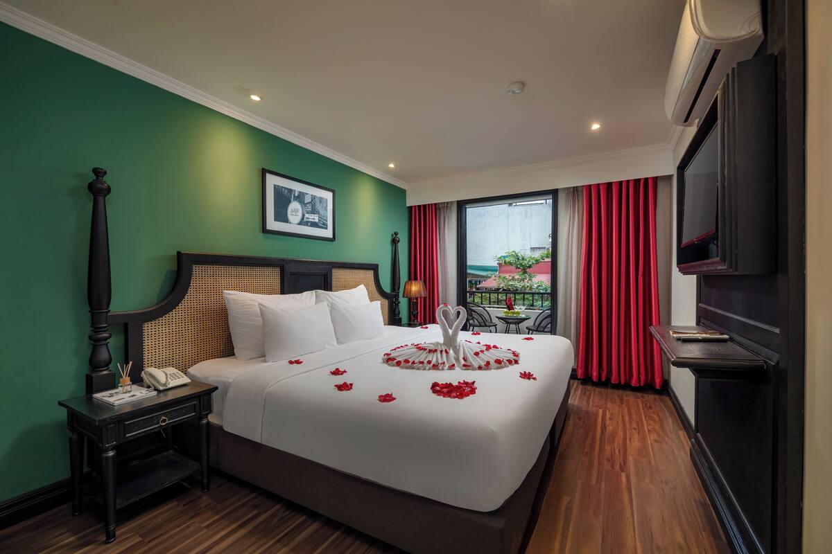 Habitación de hotel con cama, mesita de noche, lámpara, televisor y vistas al exterior.