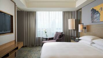 A hotel room with a large bed, a seating area with a chair, a small table with a vase, and a television on a wooden stand.