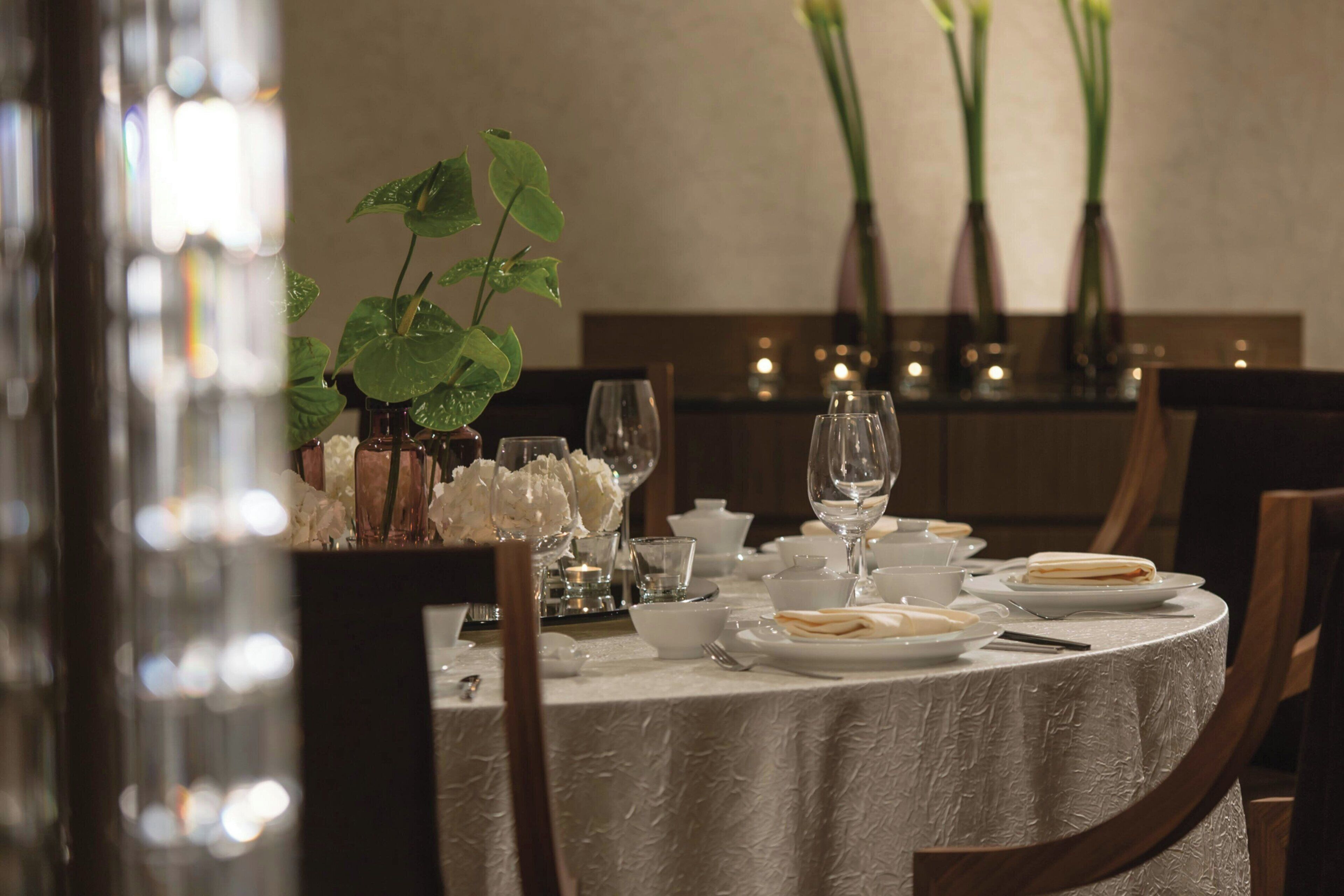 A dining table set with white tablecloth, plates, bowls, and a potted plant.