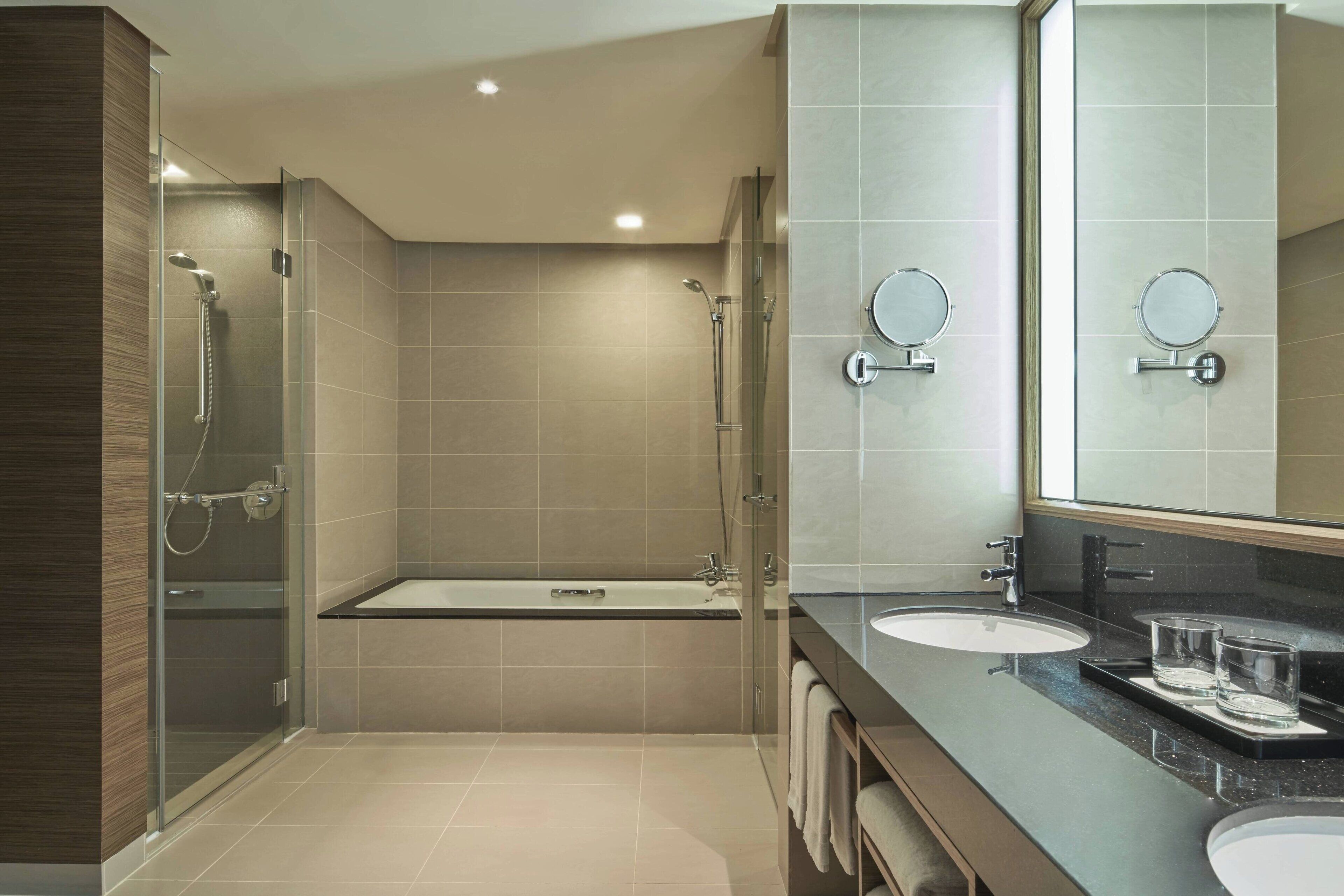 A modern bathroom with a glass-enclosed shower, a freestanding bathtub, and a vanity with two sinks and mirrors.
