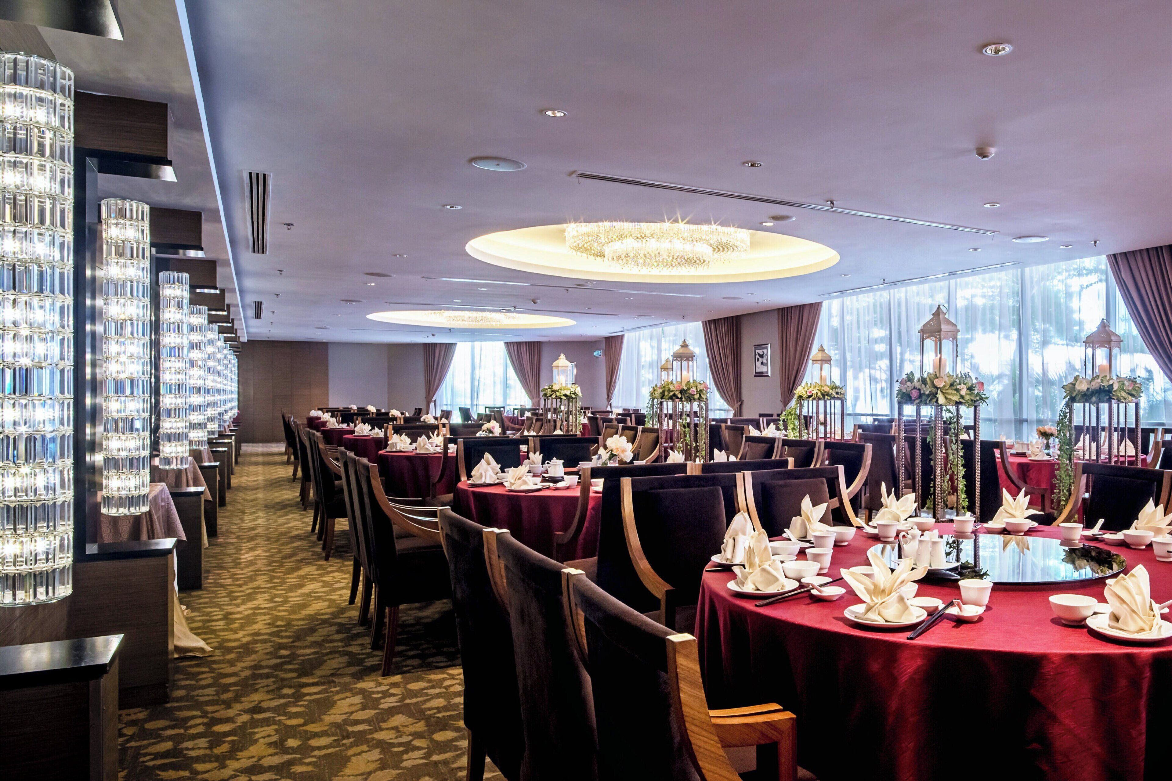 A dining area with round tables, red tablecloths, and a chandelier.
