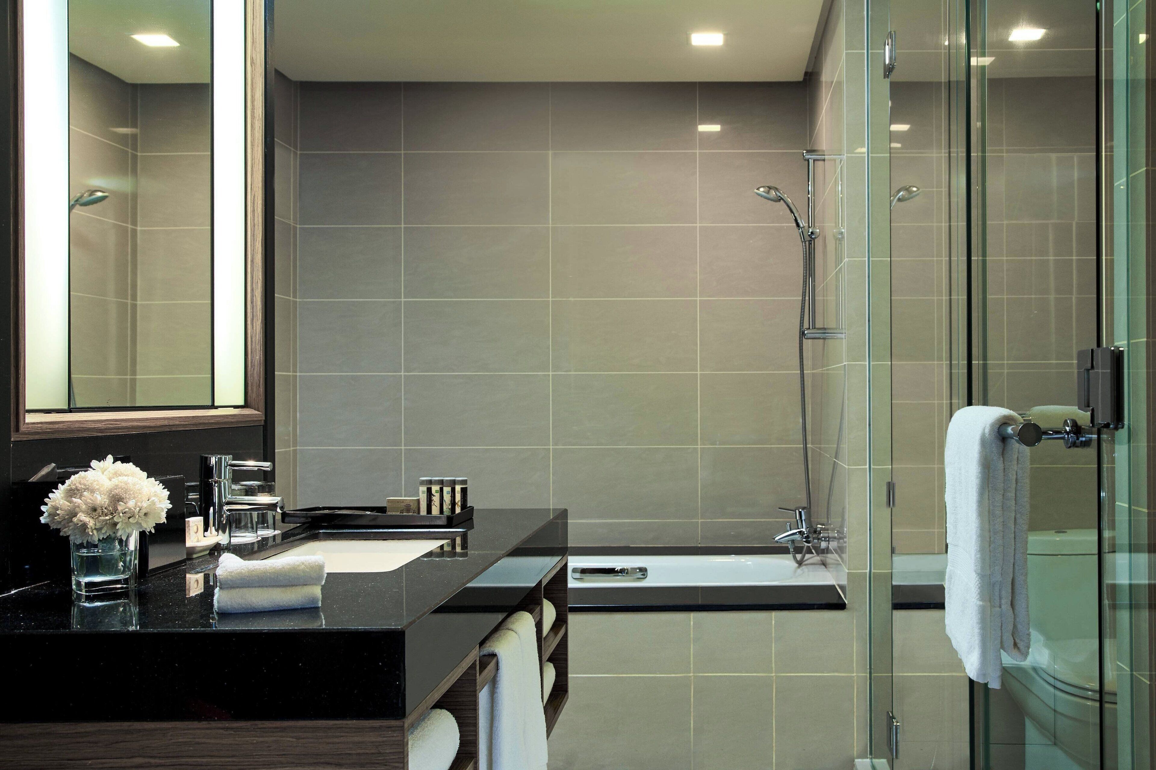 A modern bathroom with a glass shower enclosure, a black countertop, and a large mirror.