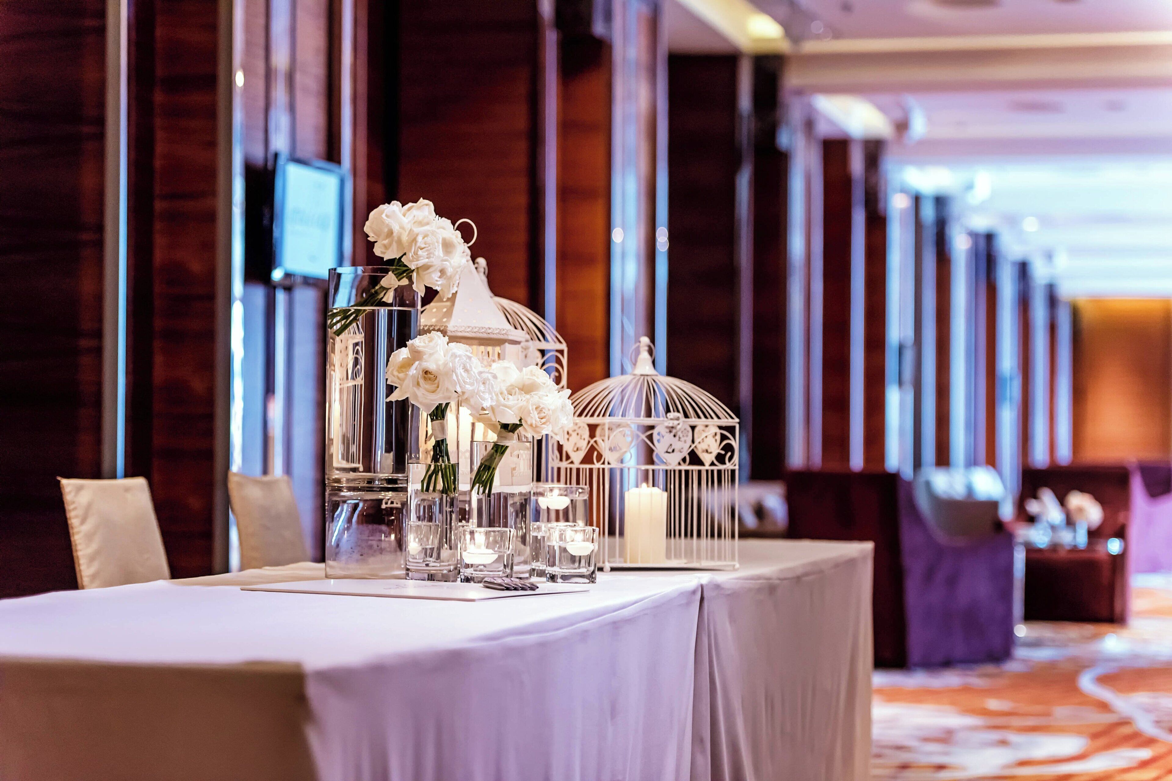 A table set with white flowers, clear glass vases, and a white birdcage.