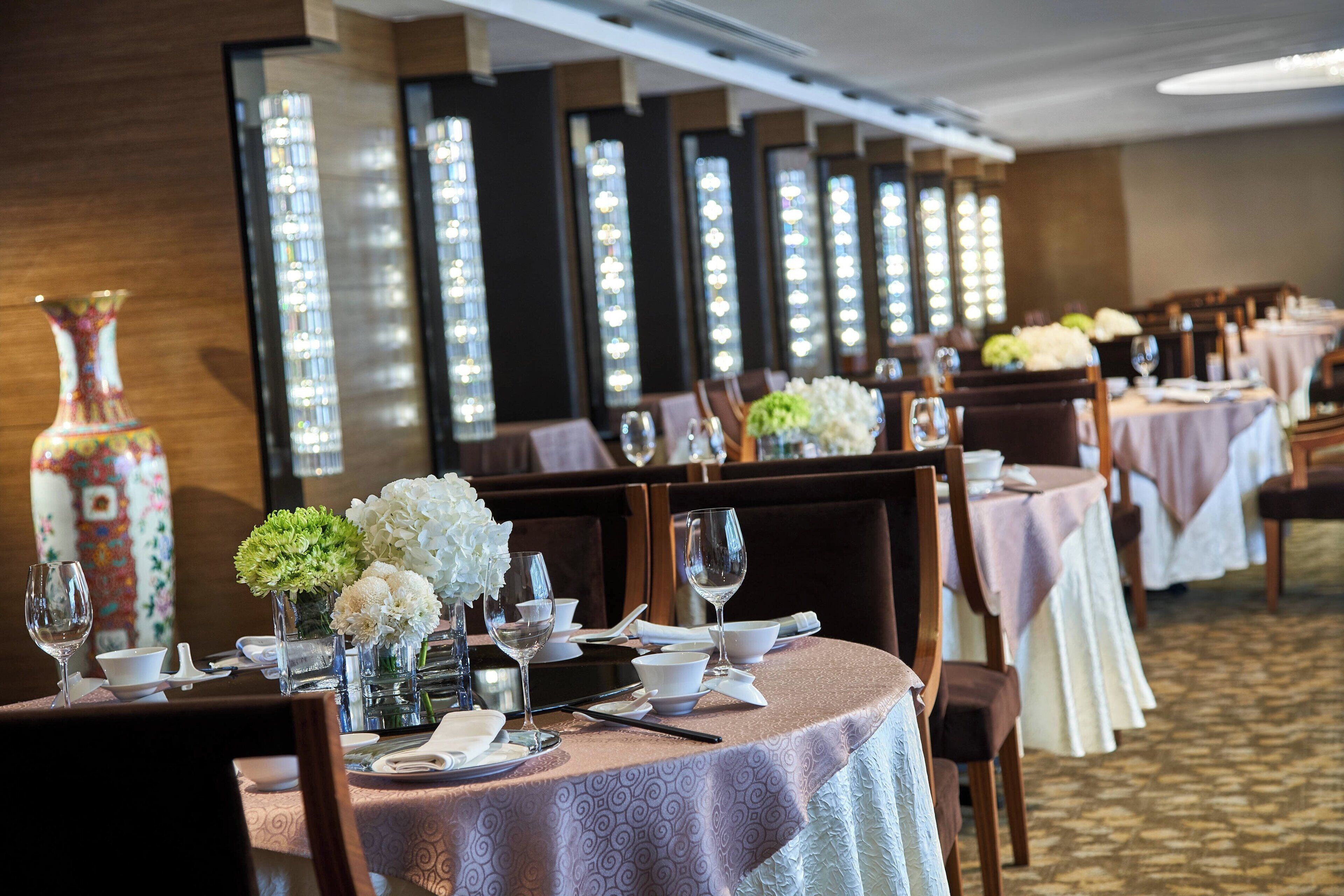A dining area with tables set for service, featuring floral centerpieces and elegant table settings.