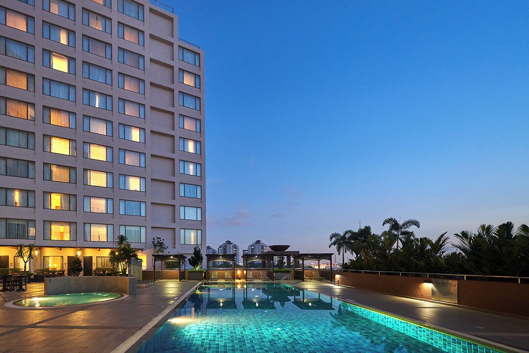 Un hotel con piscina, mobiliario exterior y vistas al horizonte urbano.
