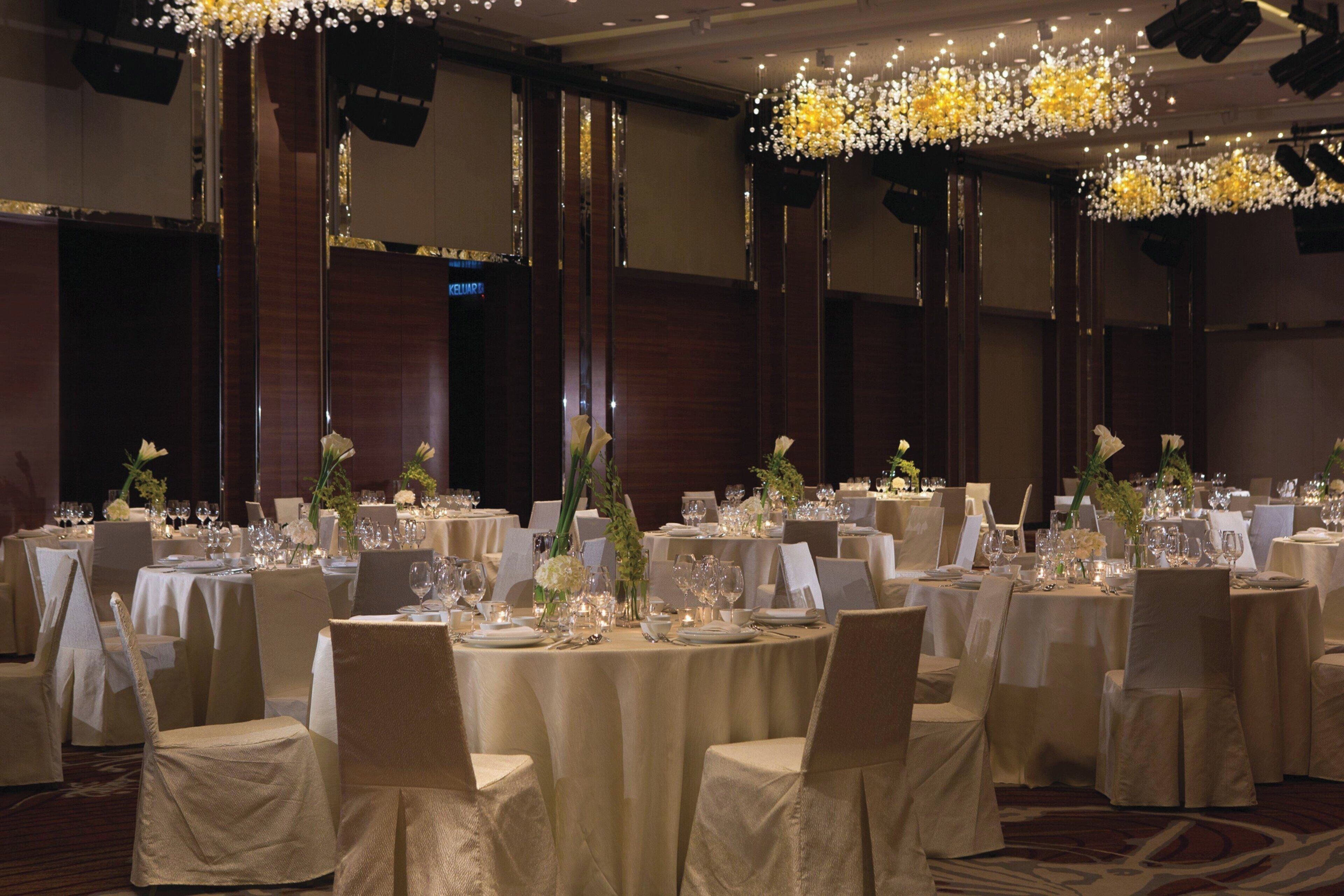 Un salón de banquetes con mesas redondas dispuestas para un evento formal, con centros de mesa florales y elegantes vajillas.