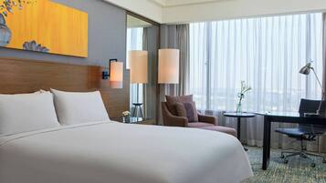 Une chambre d’hôtel avec un grand lit, un bureau, une chaise, une petite table et une grande fenêtre avec des rideaux.
