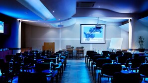 Un salón de conferencias con filas de sillas orientadas hacia una pantalla que muestra un mensaje de bienvenida para un congreso de bioquímica.