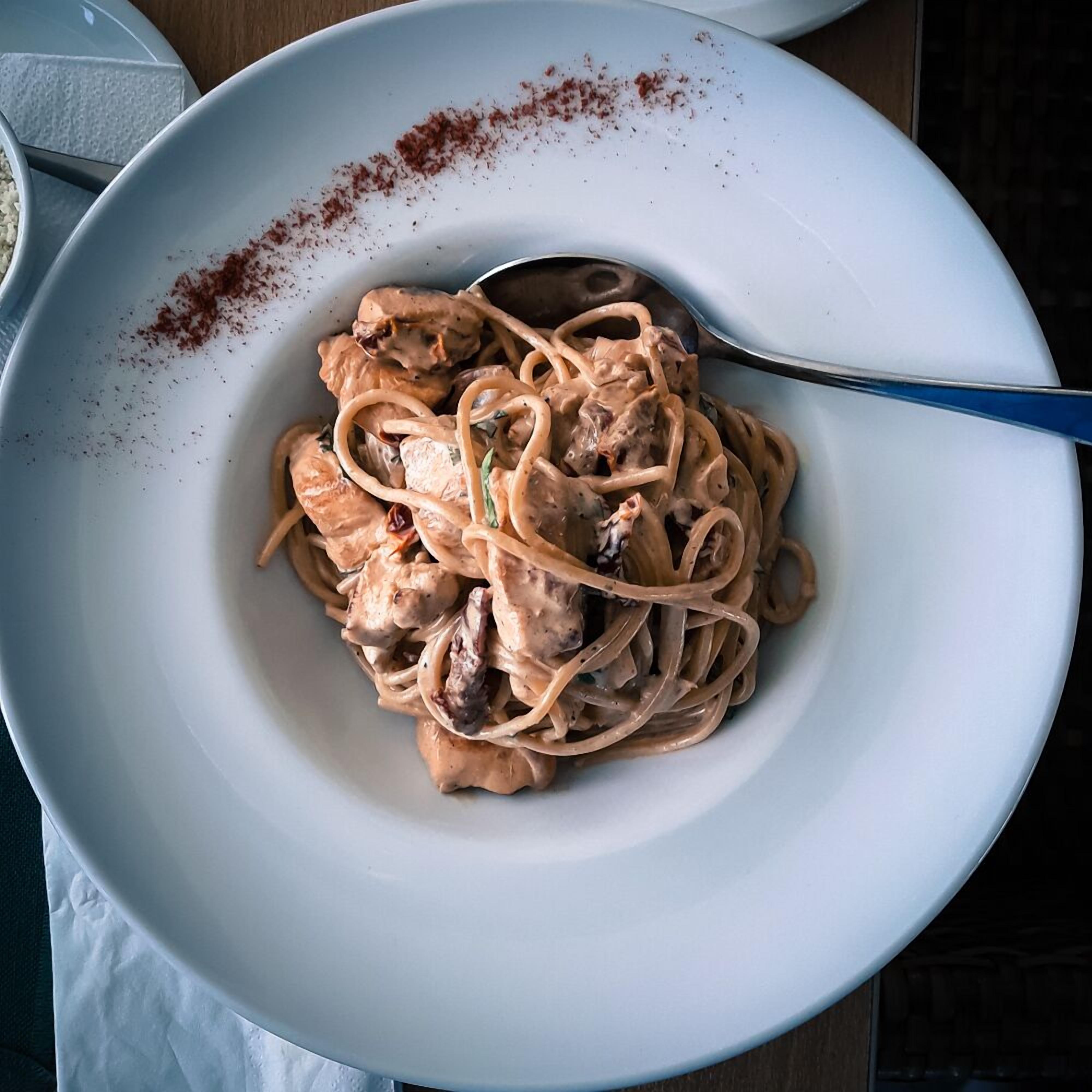 A bowl of pasta with a creamy sauce and a sprinkle of red spice on the side.