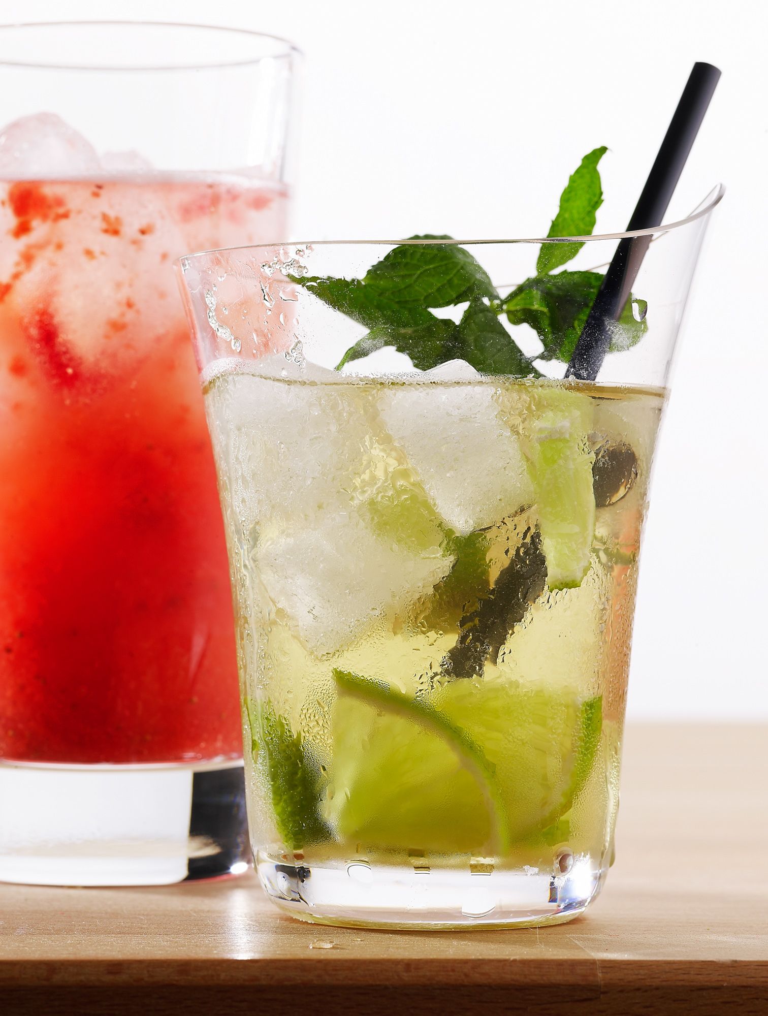 Two glasses of cocktails with ice cubes and mint leaves, one with a red drink and the other with a clear drink.