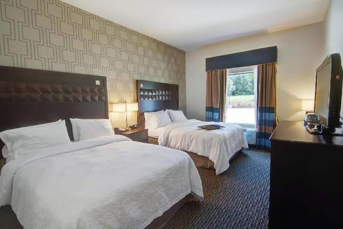 A hotel room with two beds, a TV, and a window with curtains.