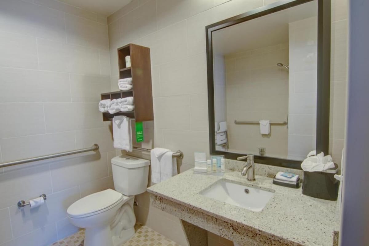 A bathroom with a toilet, sink, mirror, towel rack, and a shelf with towels.