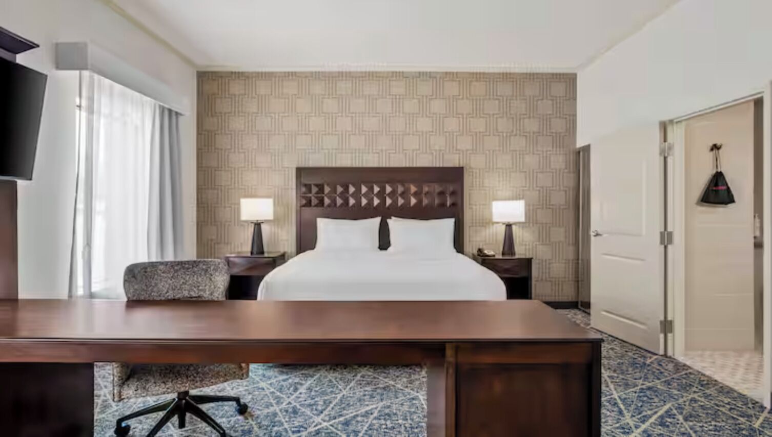 Une chambre d’hôtel avec un grand lit, deux tables de chevet avec des lampes, un bureau et une chaise.