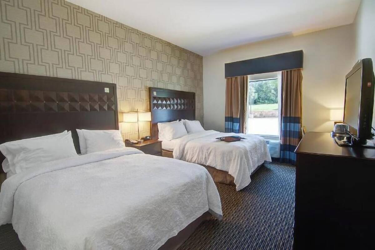A hotel room with two beds, a TV, and a window with curtains.