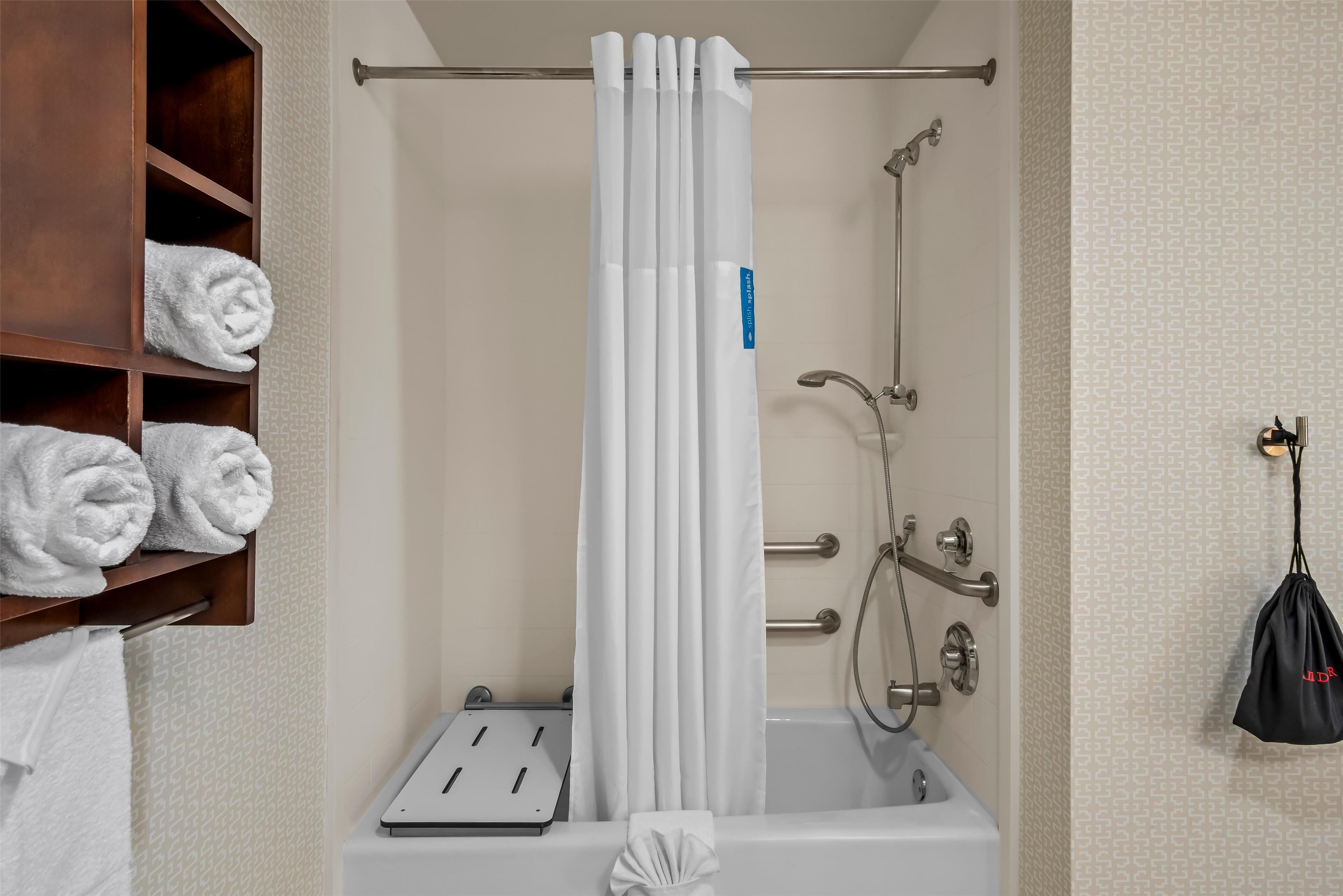 A bathroom with a shower, a towel rack with neatly folded towels, and a handheld showerhead.
