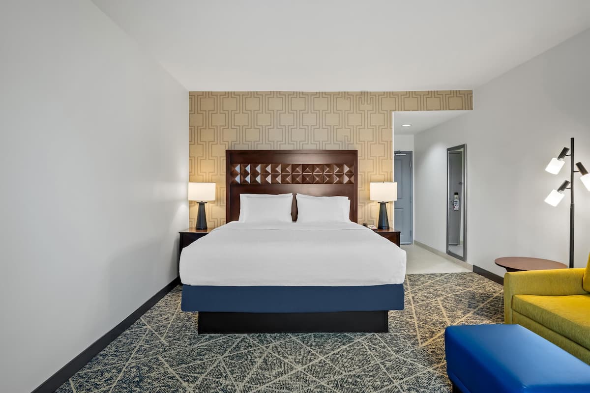 A hotel room with a large bed, two bedside tables with lamps, a patterned carpet, and a yellow armchair.
