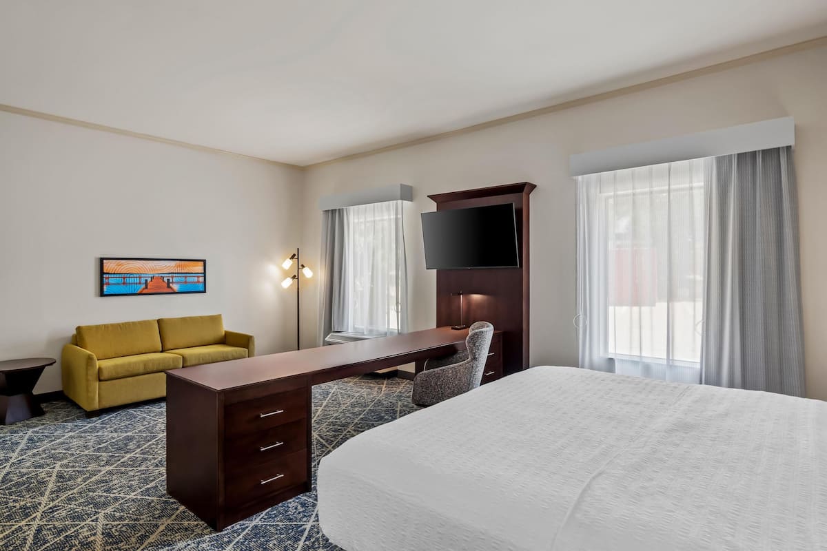 A hotel room with a bed, a desk, a sofa, a TV, and a painting on the wall.