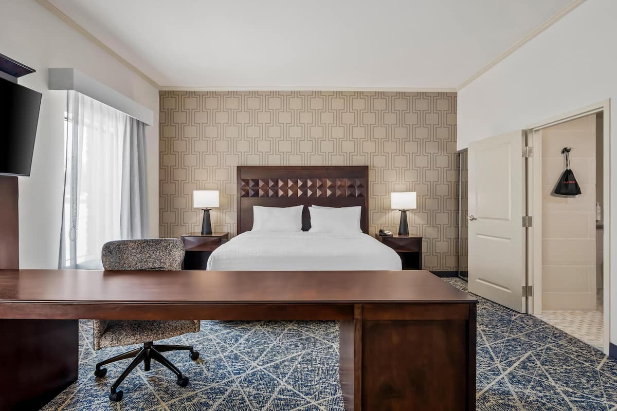 A hotel room with a large bed, two bedside tables with lamps, a desk, and a TV.