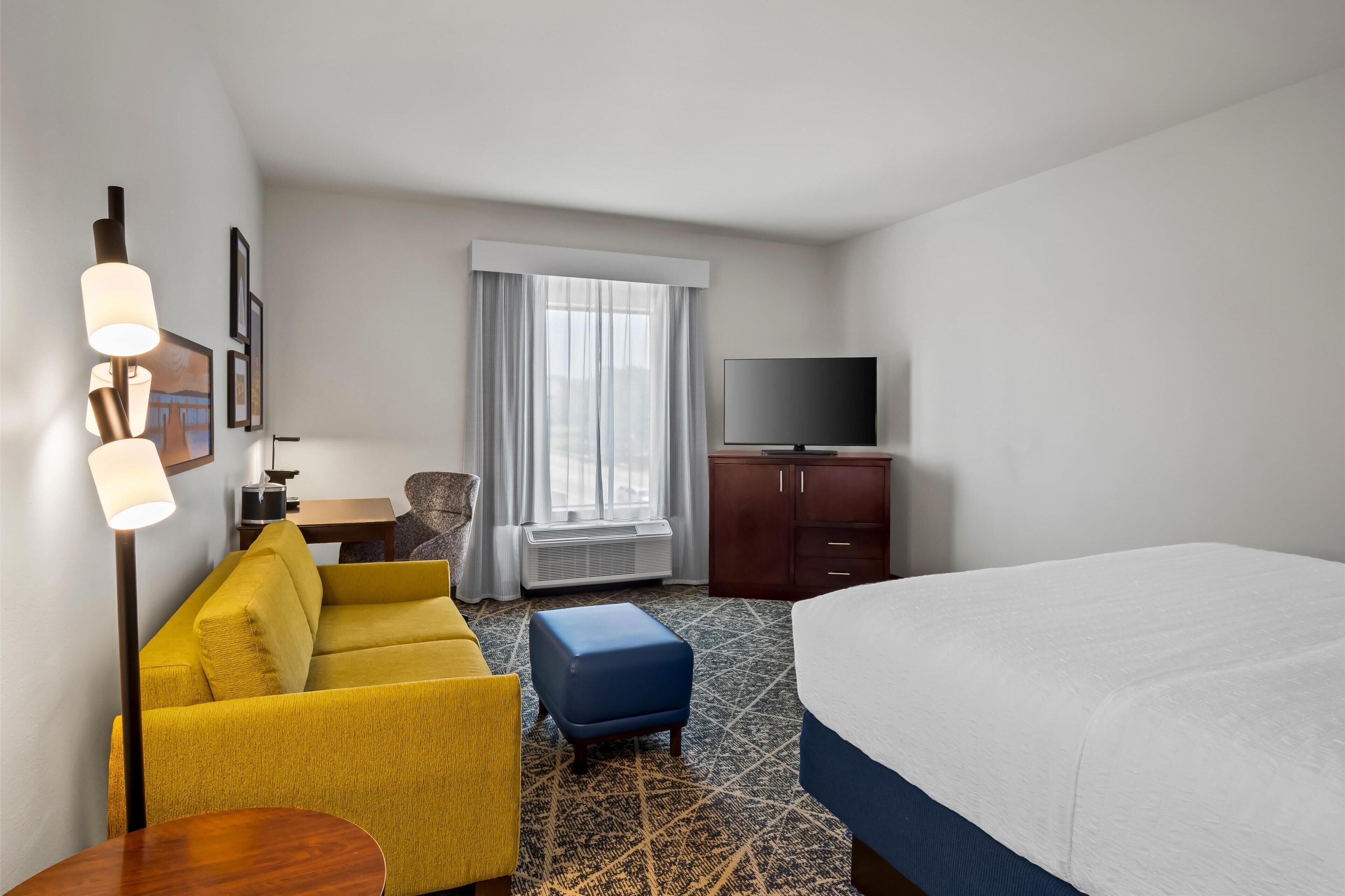 A hotel room with a bed, a sofa, a desk, a television, and a window with curtains.