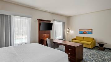 Une chambre d’hôtel avec un lit, un bureau, une chaise, un canapé, une télévision et un tableau au mur.