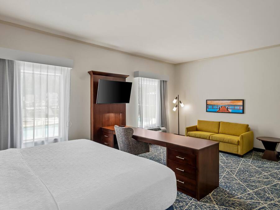 Une chambre d’hôtel avec un lit, un bureau, une chaise, un canapé, une télévision et un tableau au mur.
