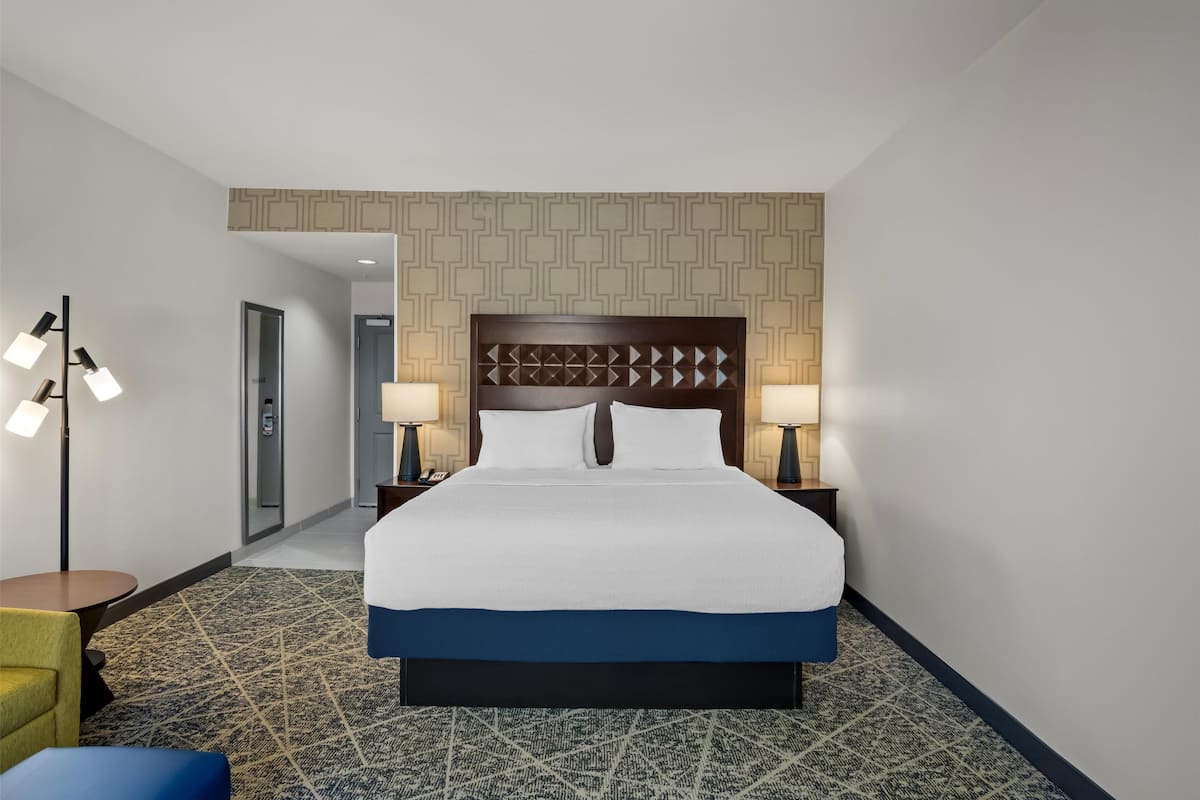 A hotel room with a large bed, two bedside tables with lamps, a patterned carpet, and a geometric wall design.