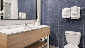 Une salle de bain moderne avec un lavabo blanc, un miroir et des toilettes. Les murs sont recouverts de carreaux disposés selon un motif géométrique.