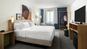 Une chambre d’hôtel avec un grand lit, une télévision, une armoire et un bureau avec une lampe.