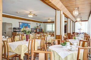 Comedor con varias mesas y sillas, ventiladores de techo y candelabros.