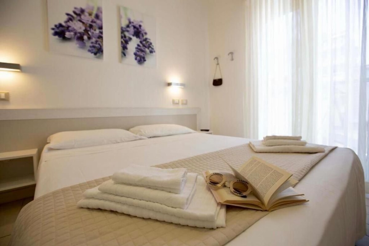A neatly made bed with folded towels, a book, and glasses on the bed.