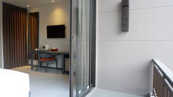 A modern hotel room with a bed, a desk with a chair, a TV mounted on the wall, and a balcony with a railing.