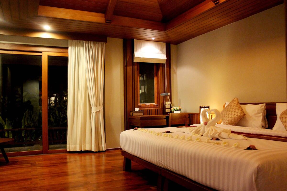 Une chambre d’hôtel dotée d’un grand lit, d’une tête de lit en bois, d’une table de chevet et d’une porte-fenêtre coulissante donnant sur un espace extérieur.