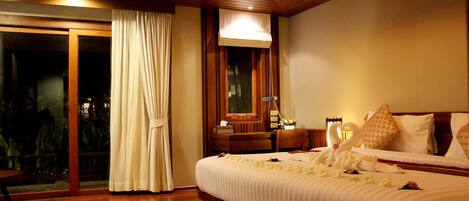 A hotel room with a large bed, a wooden headboard, a nightstand, and a sliding glass door leading to an outdoor area.