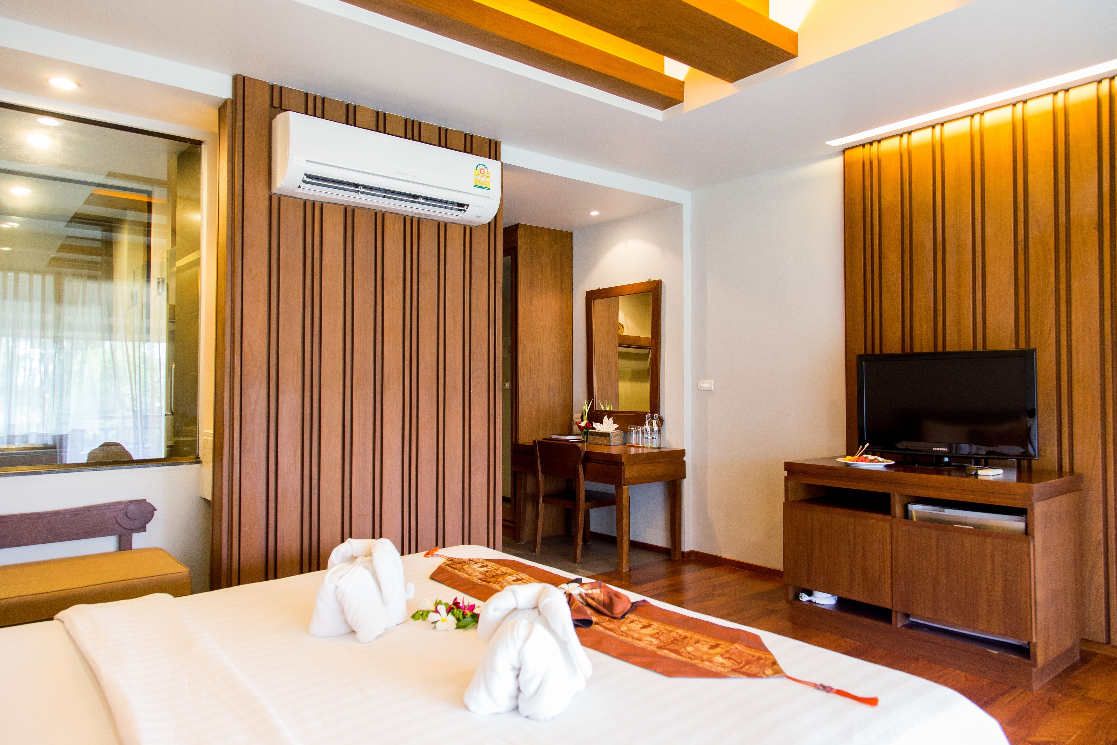 A hotel room with a bed, a desk, a television, and an air conditioning unit.