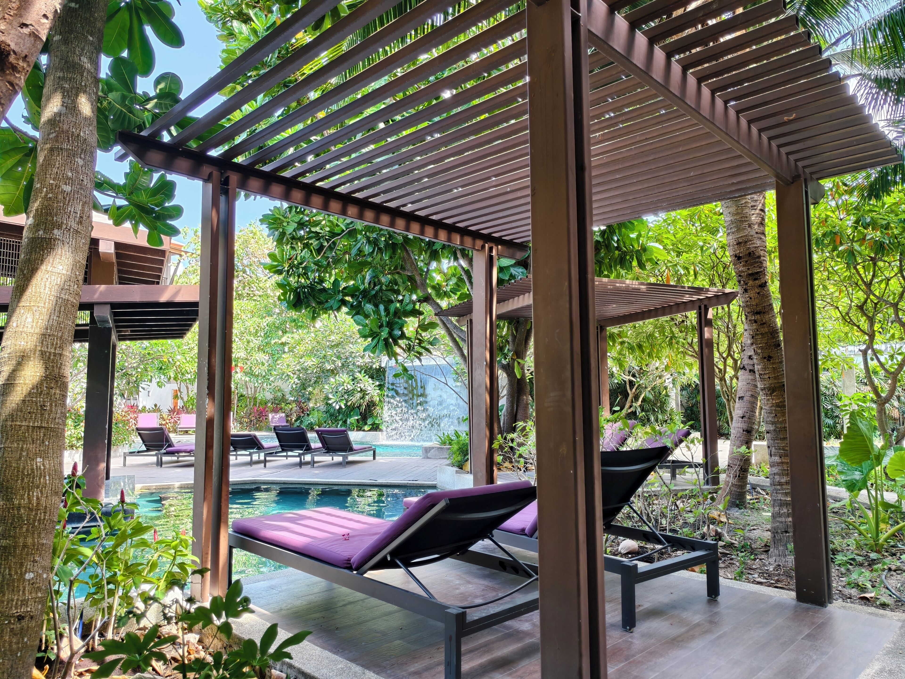 A covered outdoor area with lounge chairs and a pool.