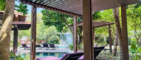 A covered outdoor area with lounge chairs and a pool.