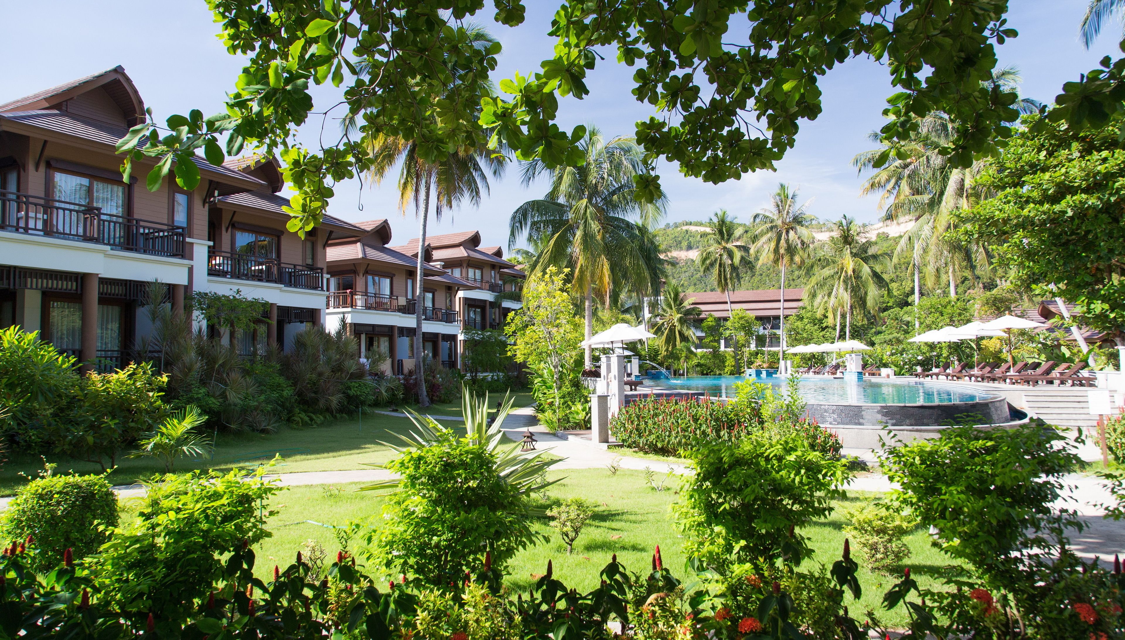 A resort with multiple-story buildings, a swimming pool, and lush greenery.