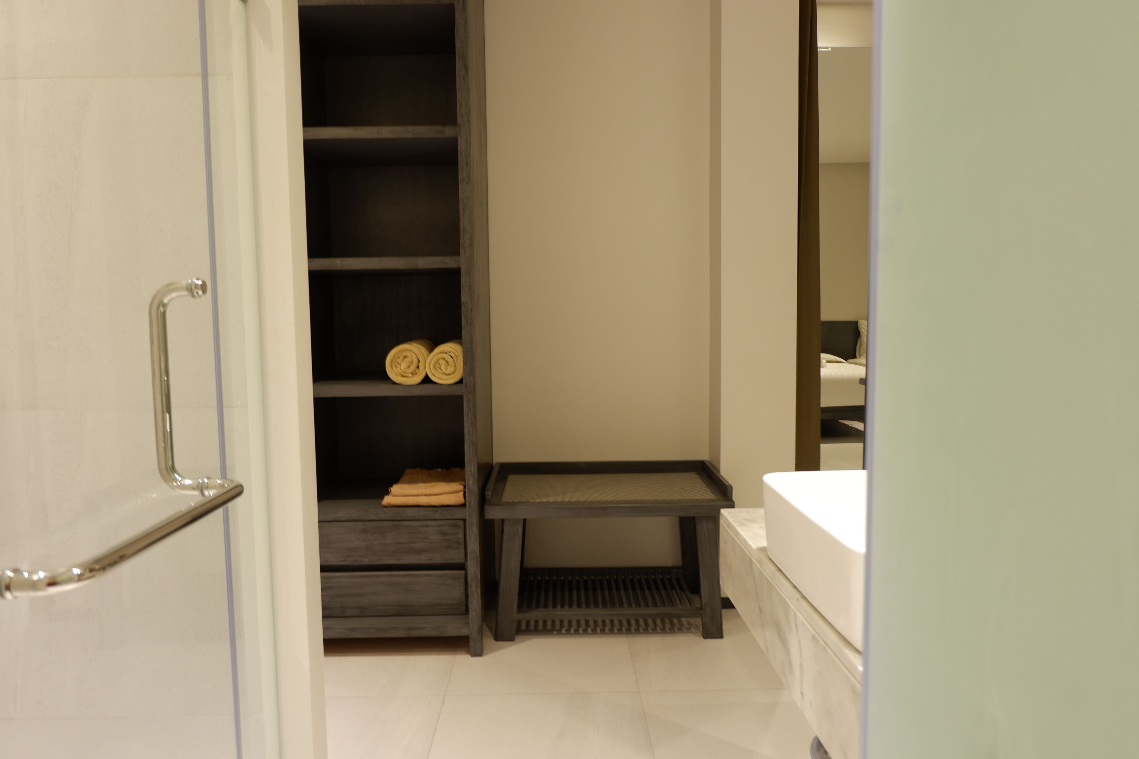 A bathroom with a shower, a toilet, and a sink. There is a towel rack and a shelf with towels.