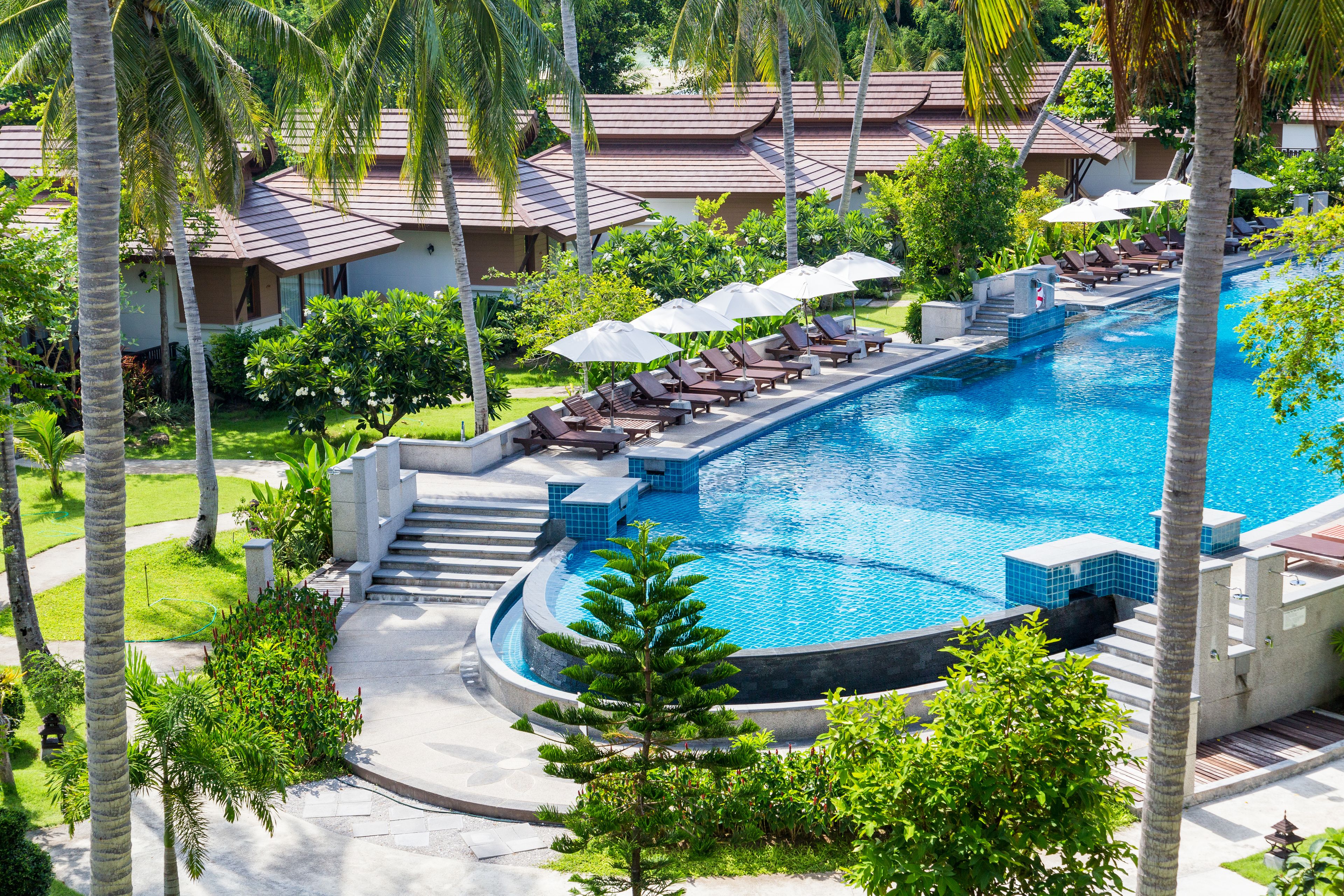 A resort with a large pool, lounge chairs, umbrellas, and palm trees.